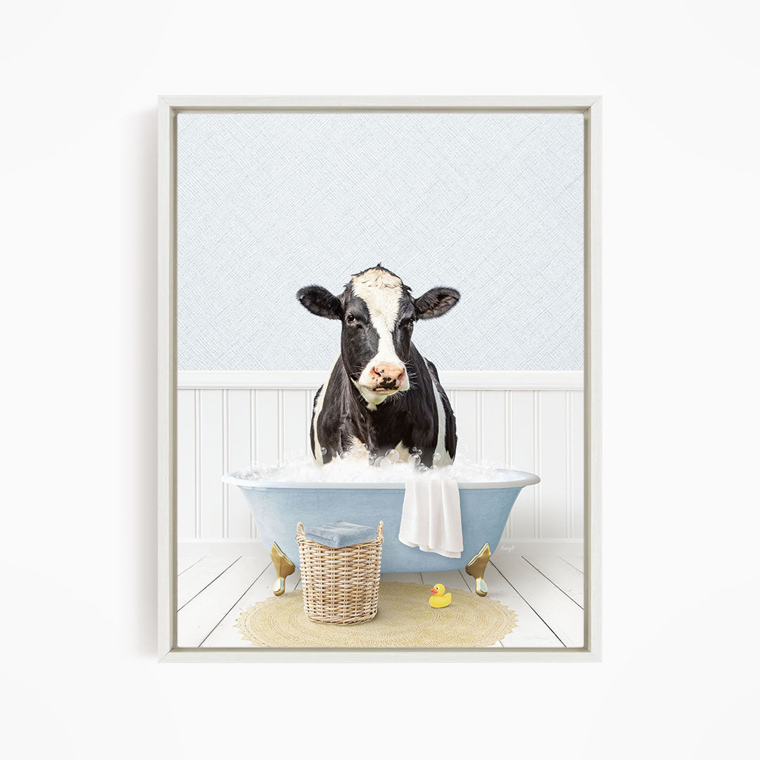 A black and white cow is sitting in a blue bathtub filled with water, surrounded by a yellow rubber duck and a basket.