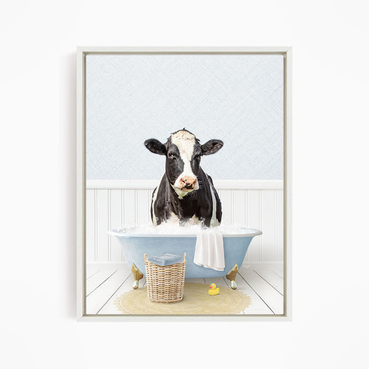 A black and white cow is sitting in a blue bathtub filled with water, surrounded by a yellow rubber duck and a basket.