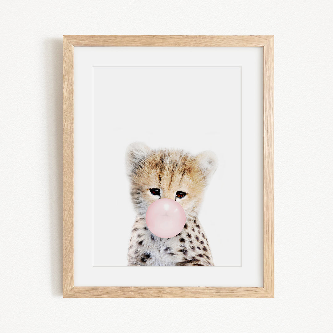 A framed image of a cheetah blowing a bubble with a pink bubble gum bubble.