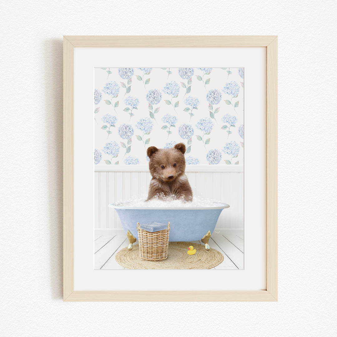 A brown bear sitting in a blue bathtub filled with bubbles, surrounded by a floral patterned wall and a basket of rubber ducks.