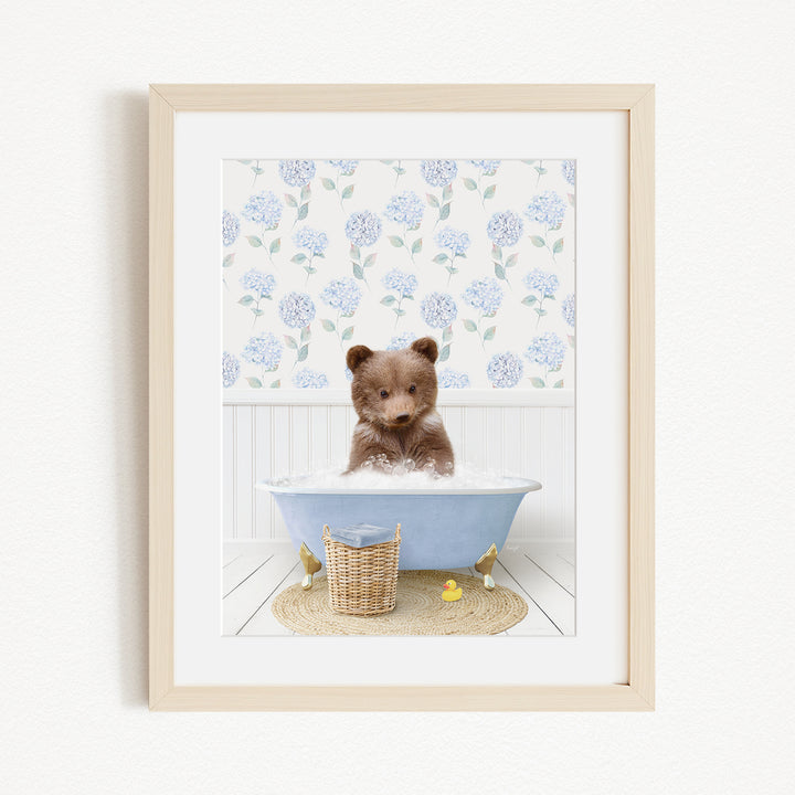 A brown bear sitting in a blue bathtub filled with bubbles, surrounded by a floral patterned wall and a basket of rubber ducks.