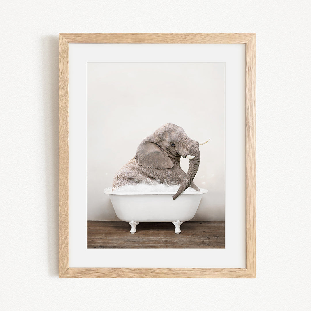 A gray elephant is sitting in a white bathtub, with its trunk raised and appearing to be enjoying the bath.