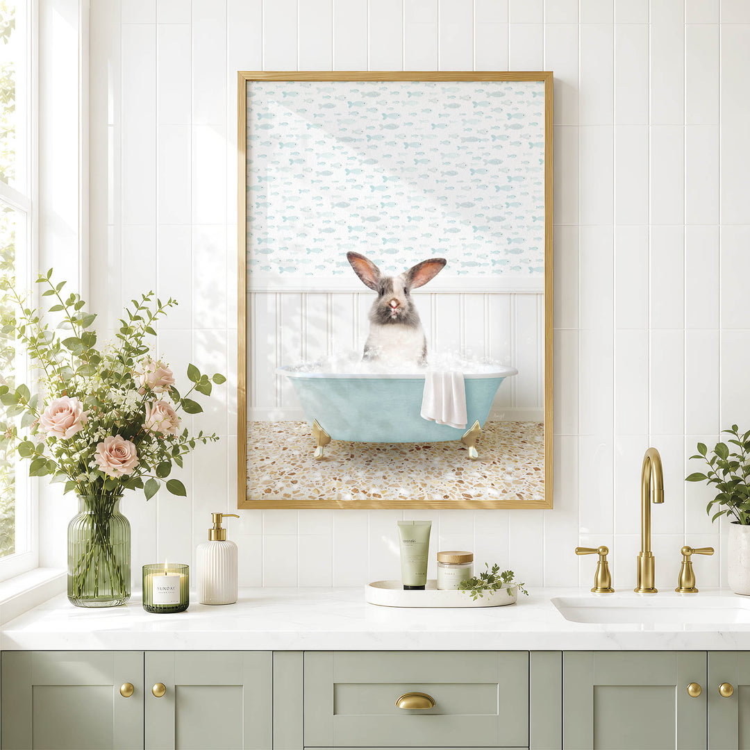 A framed image of a rabbit sitting in a bathtub, surrounded by flowers and a green vase, is displayed on a white tiled wall above a bathroom sink.