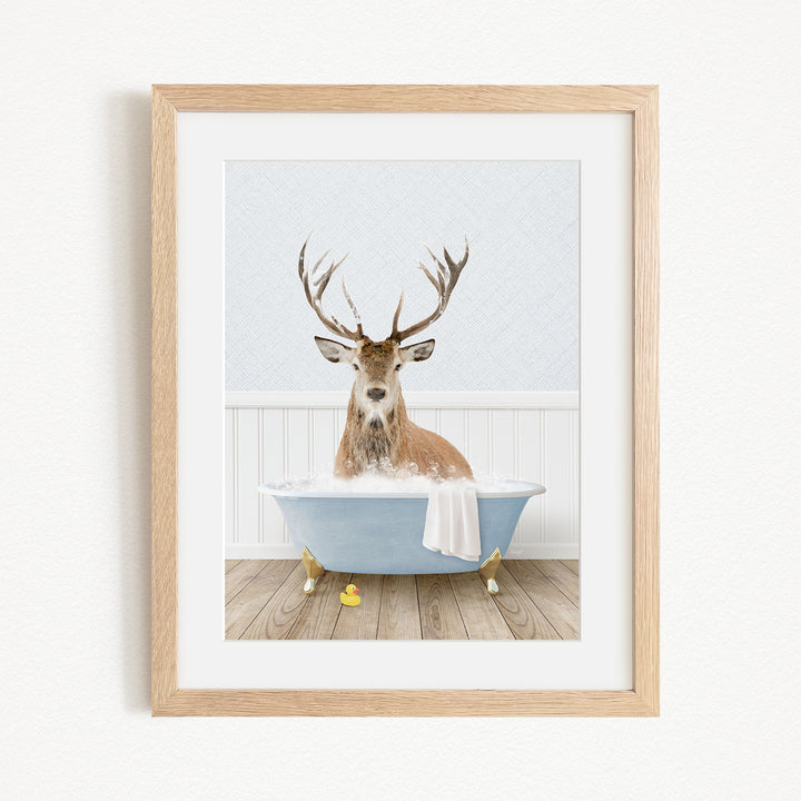 A deer with antlers is sitting in a blue bathtub filled with water, surrounded by rubber duckies.