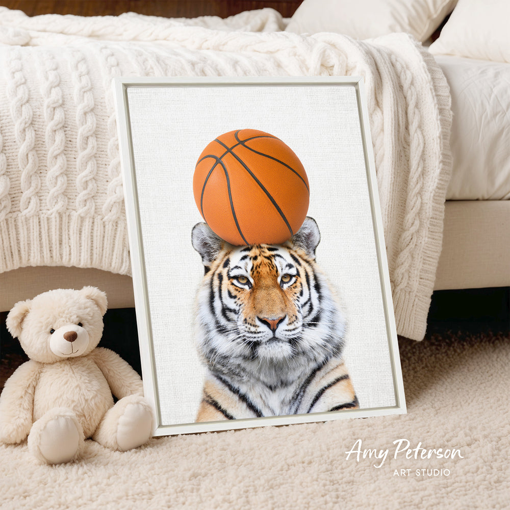 A framed print of a tiger's face with a basketball on its head is displayed on a bed, accompanied by a teddy bear.