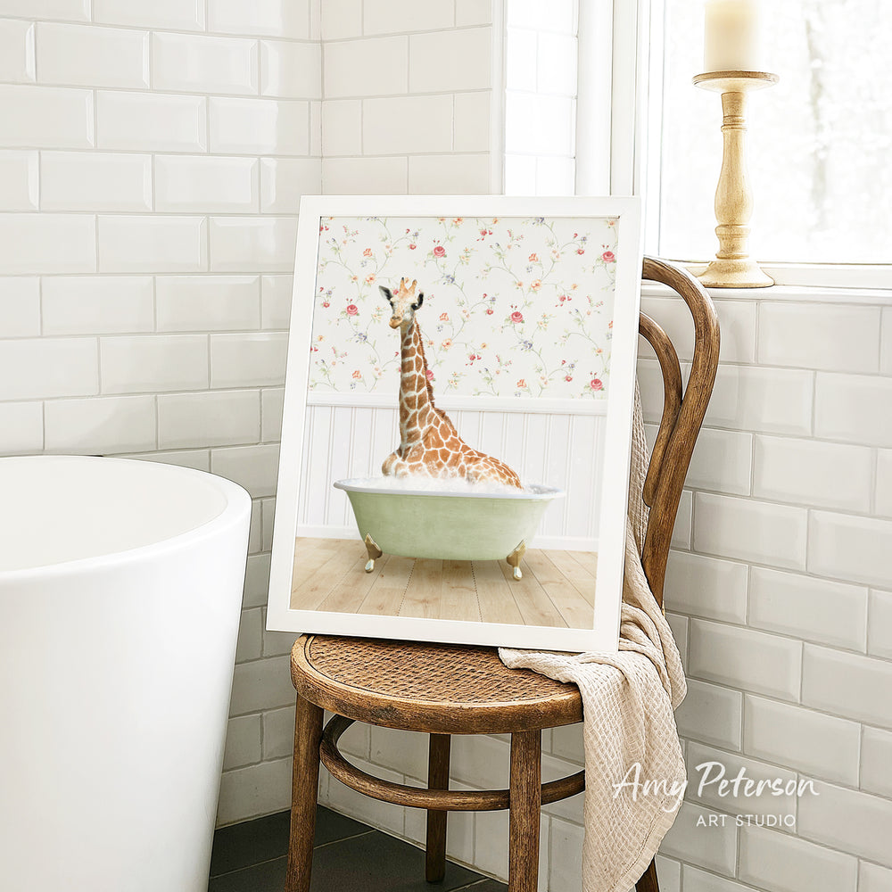 A framed image of a giraffe sitting in a bathtub is displayed on a wooden chair in a bathroom setting.