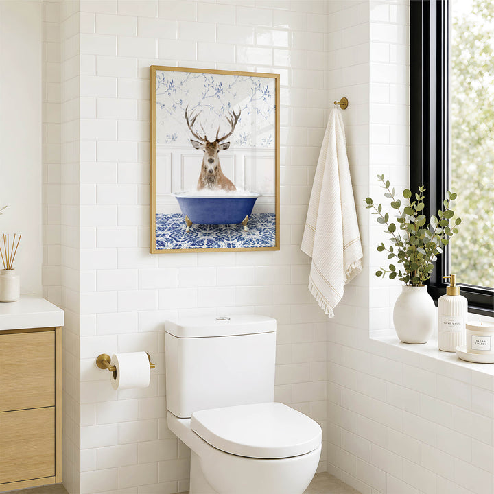 a bathroom with a white toilet, a framed picture of a deer in a bathtub, and a window with greenery outside.