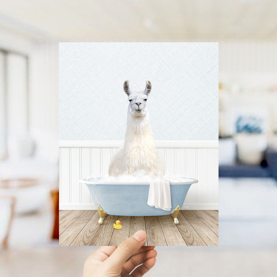 A white llama sitting in a blue bathtub filled with bubbles, with a yellow rubber duck floating nearby.