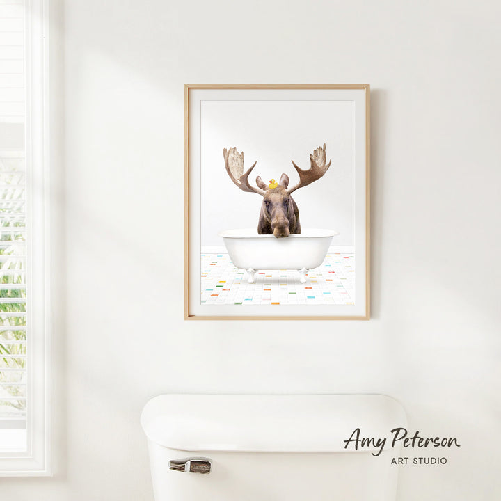 A framed image of a moose sitting in a bathtub, with its large antlers and a yellow rubber duck floating in the water.