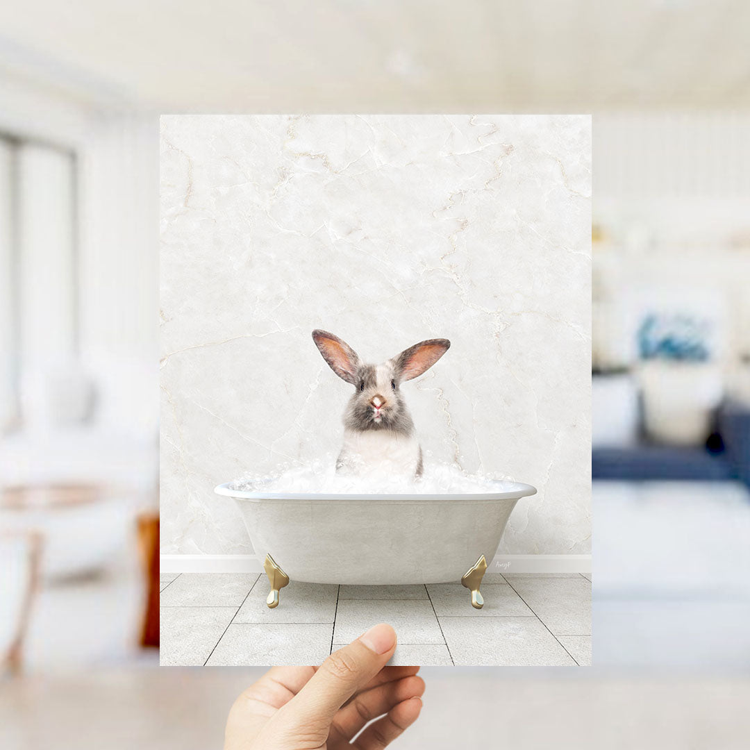 A hand holds up a framed image of a rabbit sitting in a bathtub filled with water, looking directly at the camera.