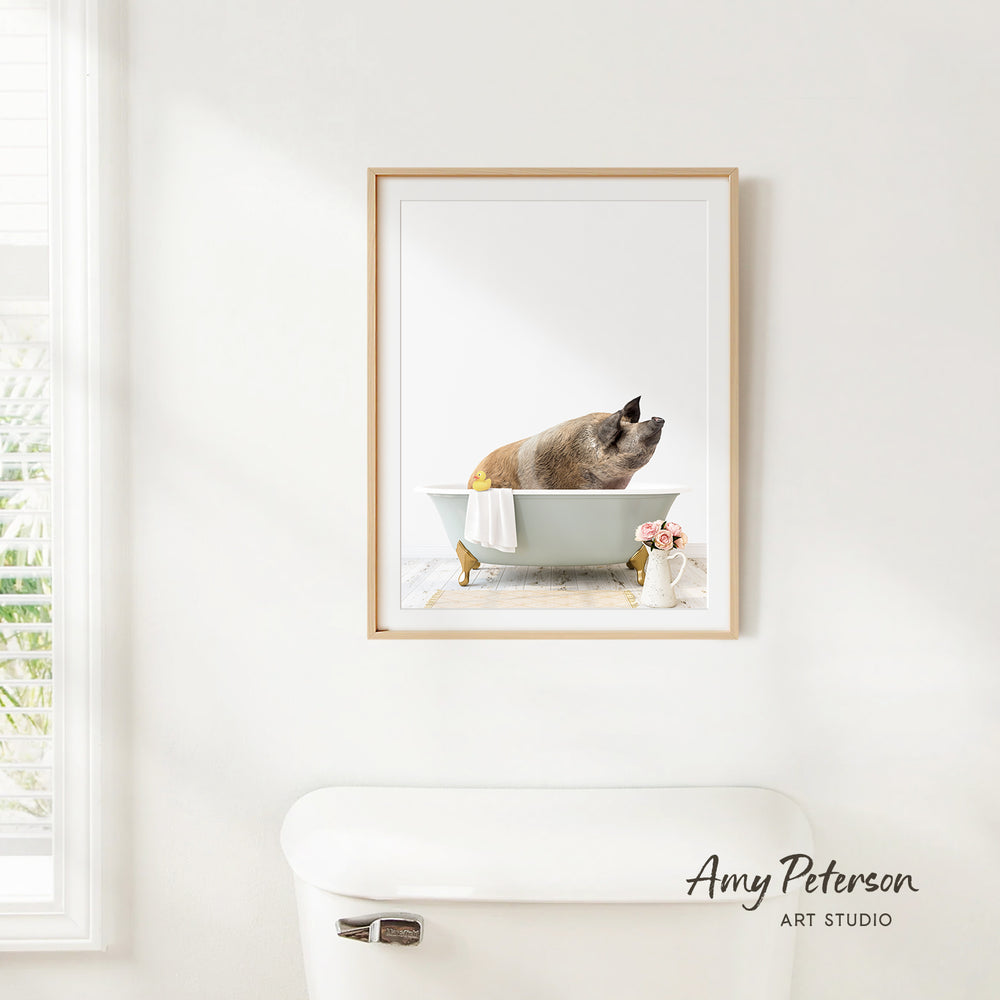 A framed image of a pig sitting in a bathtub, with a vase of flowers and a white toilet visible in the background.
