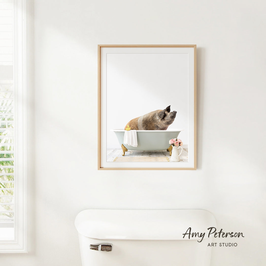 A framed image of a pig sitting in a bathtub, with a vase of flowers and a white toilet visible in the background.