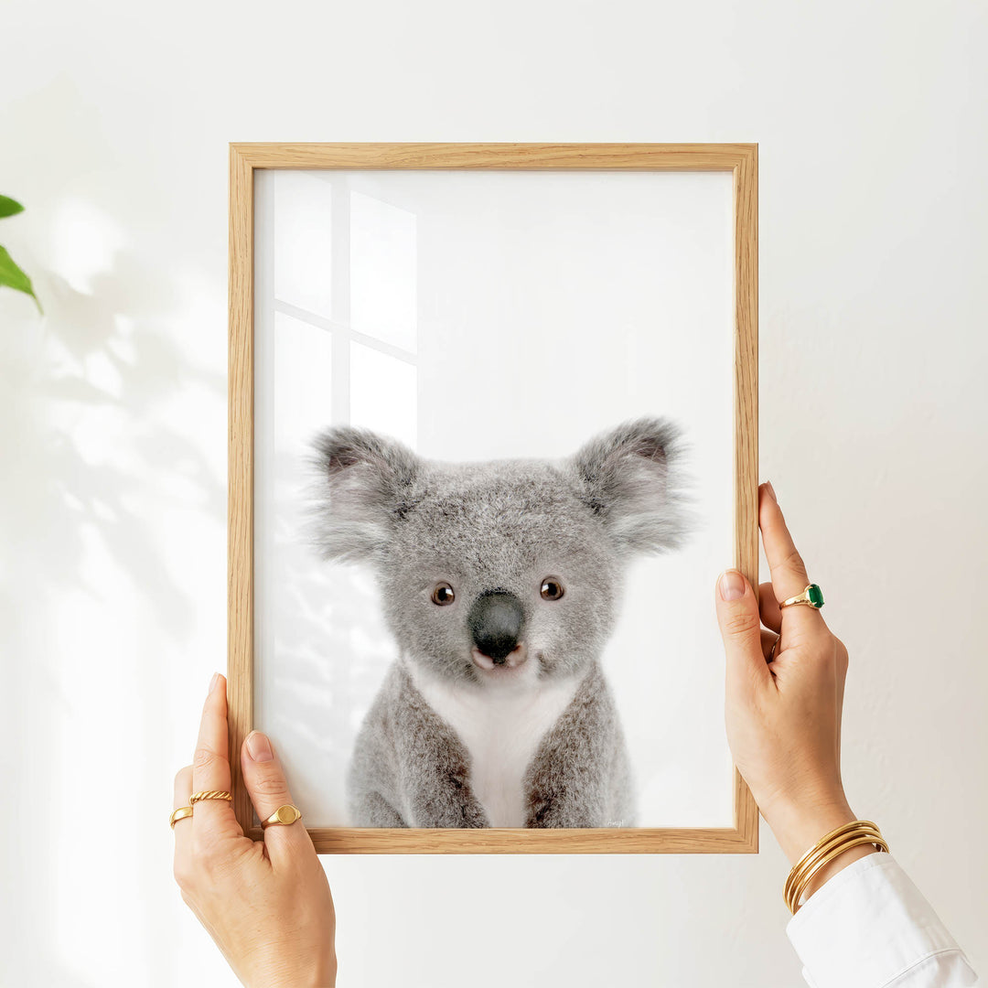 A person's hands are holding a wooden frame with a picture of a koala inside it.