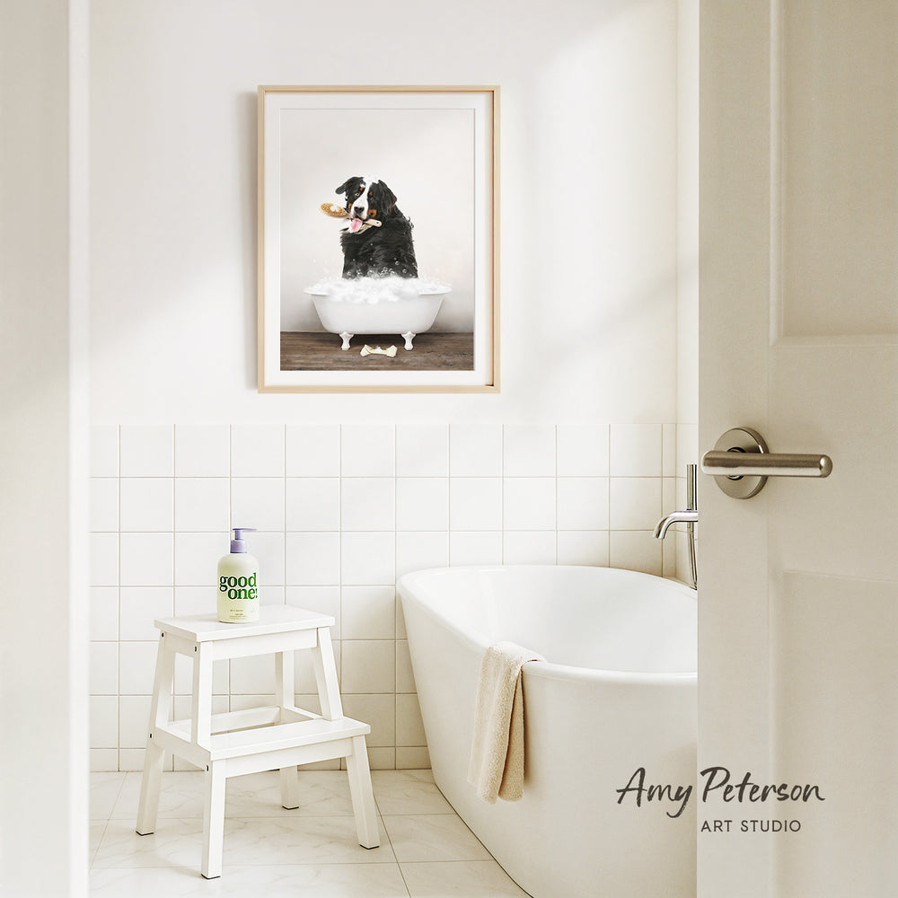 A framed image of a dog sitting in a bathtub, with a towel draped over the side of the tub, is displayed on the wall above a white bathtub in a clean, white-tiled bathroom.