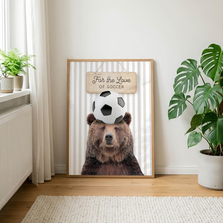 A framed poster featuring a brown bear with a soccer ball on its head, along with the text "For the Love of Soccer".