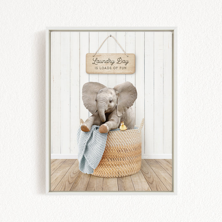 A framed image of a baby elephant sitting in a woven laundry basket, with a sign above that says "Laundry Day is loads of fun".