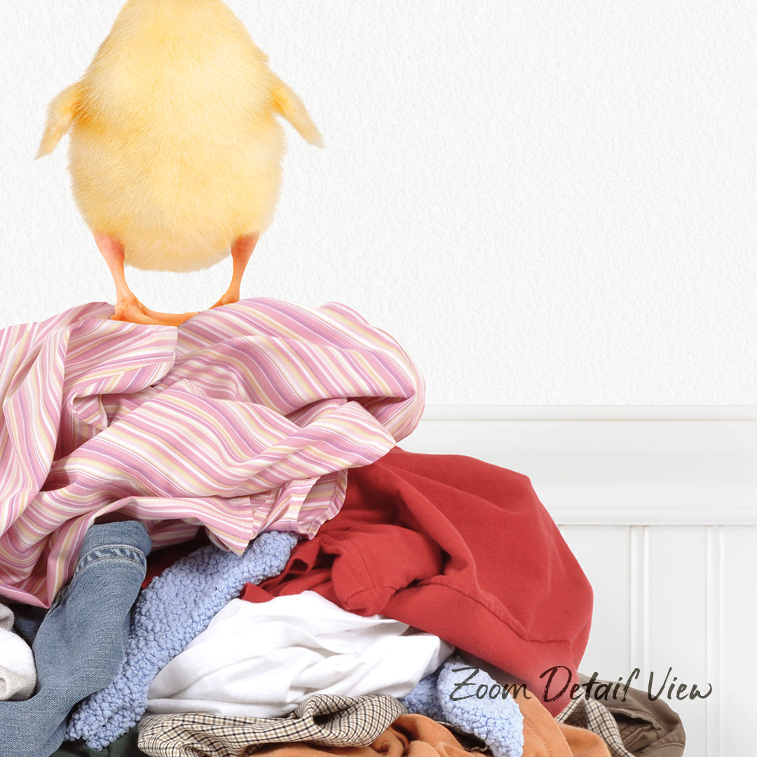 A yellow chick stands atop a pile of clothes, pecking at the fabric.