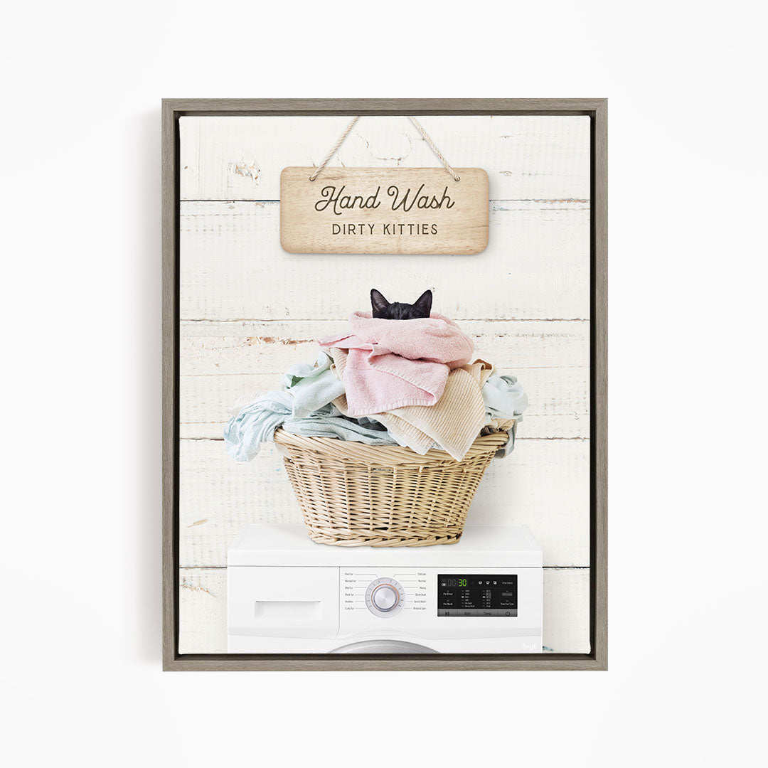 A framed image depicting a cat sitting in a basket filled with laundry, with a sign above that reads "Hand Wash Dirty Kittens".