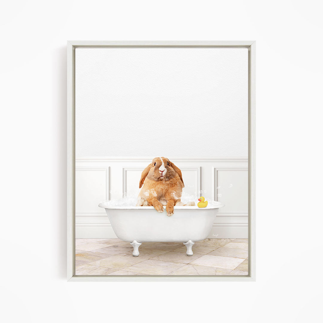 A brown rabbit sitting in a white bathtub filled with bubbles, with a rubber duck floating in the water.