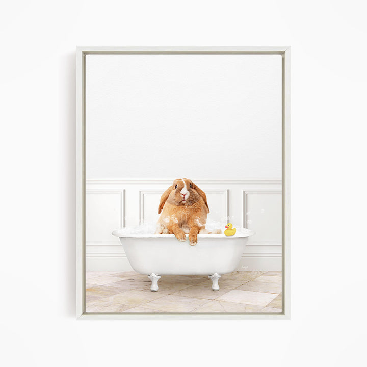 A brown rabbit sitting in a white bathtub filled with bubbles, with a rubber duck floating in the water.