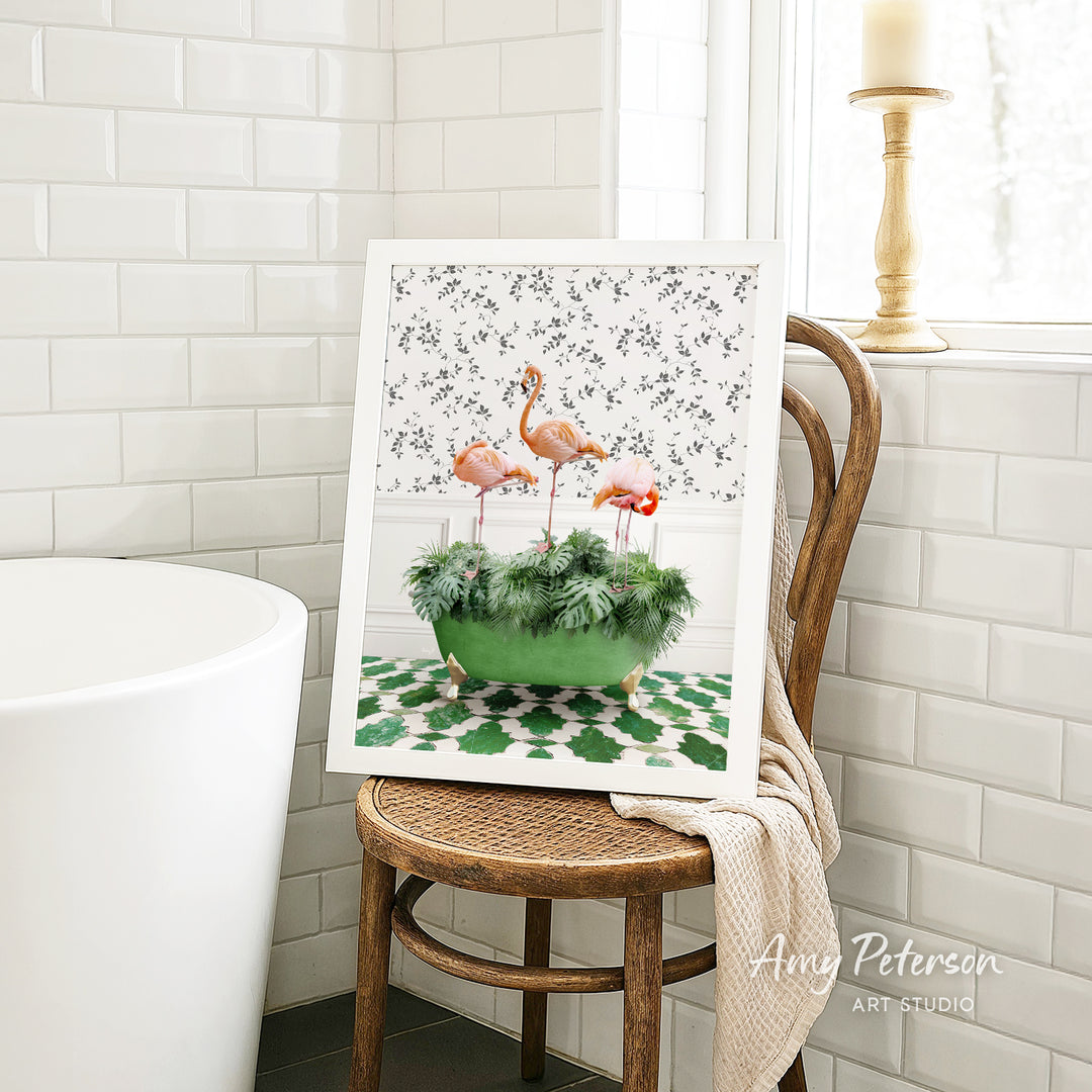 A framed print of a flamingo in a green pot is displayed on a wooden chair in a bathroom setting.