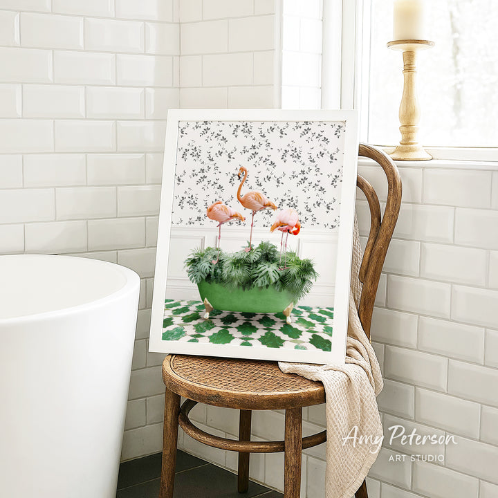 A framed print of a flamingo in a green pot is displayed on a wooden chair in a bathroom setting.