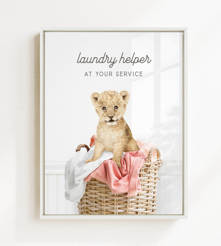 A young lion cub sitting in a wicker basket filled with clothes, with the text "laundry helper at your service" displayed above the image.