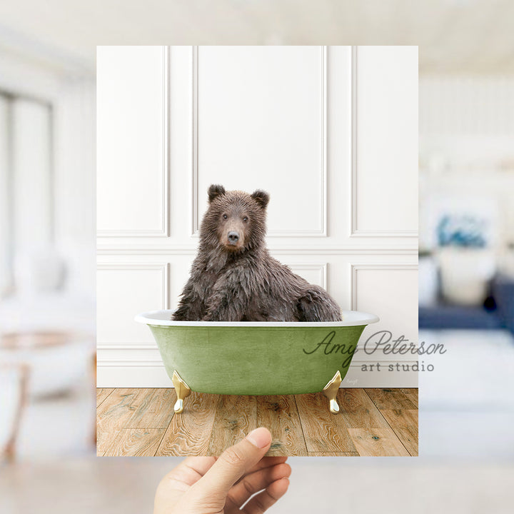 a hand holding a photo of a bear in a bathtub