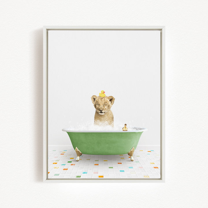 A young lion cub is sitting in a green bathtub filled with bubbles, with a yellow duck perched on its head.