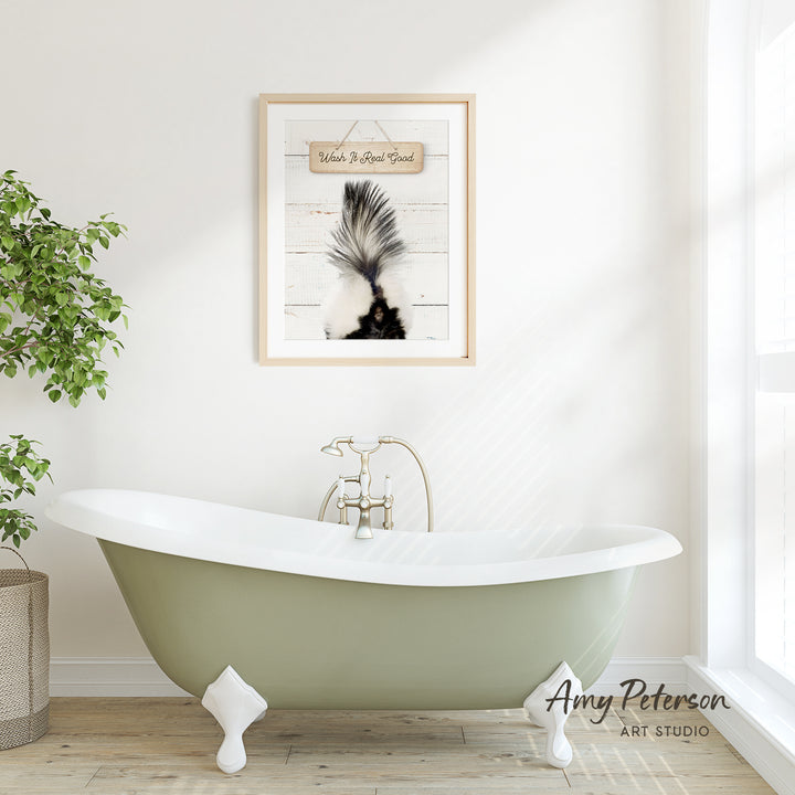 a green clawfoot bathtub with a framed picture of a skunk above it, hanging on a white wall.