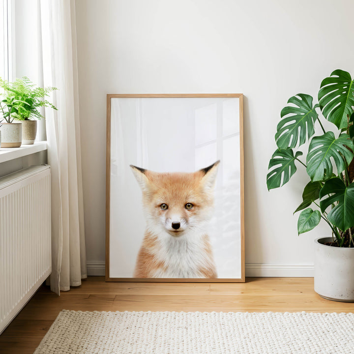 a framed photograph of a fox, which is the main focus of the room. The fox is sitting in front of a window, and there are two potted plants in the room, one on the left side and the other on the right side. The overall setting appears to be a cozy and comfortable indoor space.