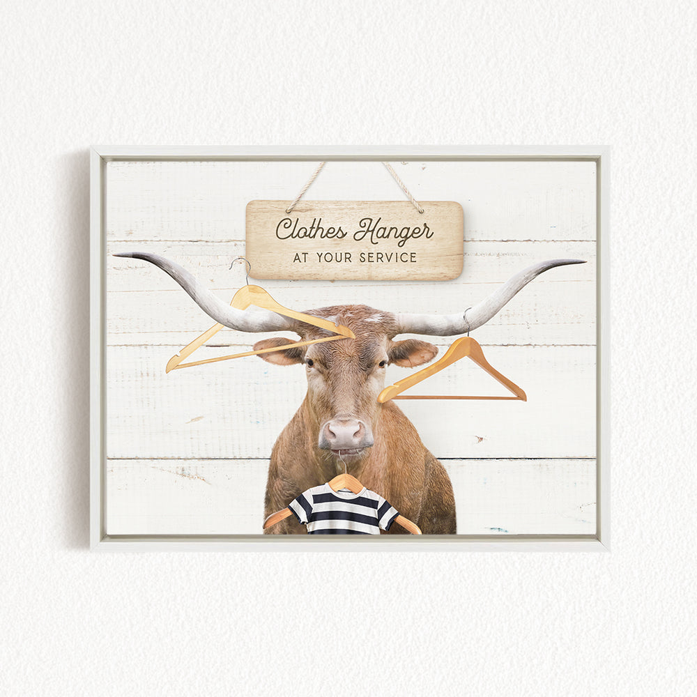 A bull with large horns is standing in front of a wooden sign that says "Clothes Hanger at your service".