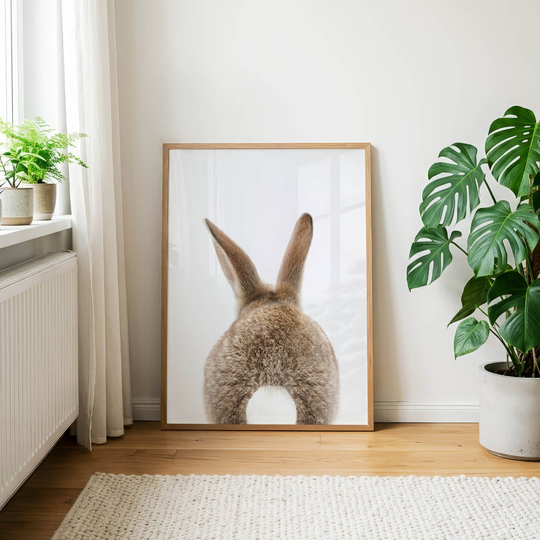 a large picture of a rabbit's back, with its long ears and fluffy tail, displayed on a wall in a room with a rug and potted plants.