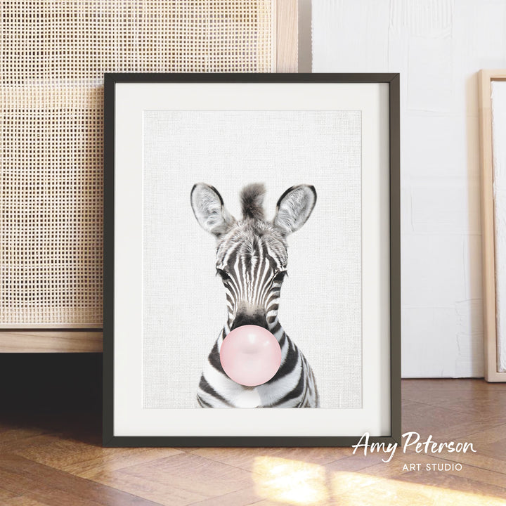 A framed print of a zebra blowing a bubble with a pink bubble gum bubble.