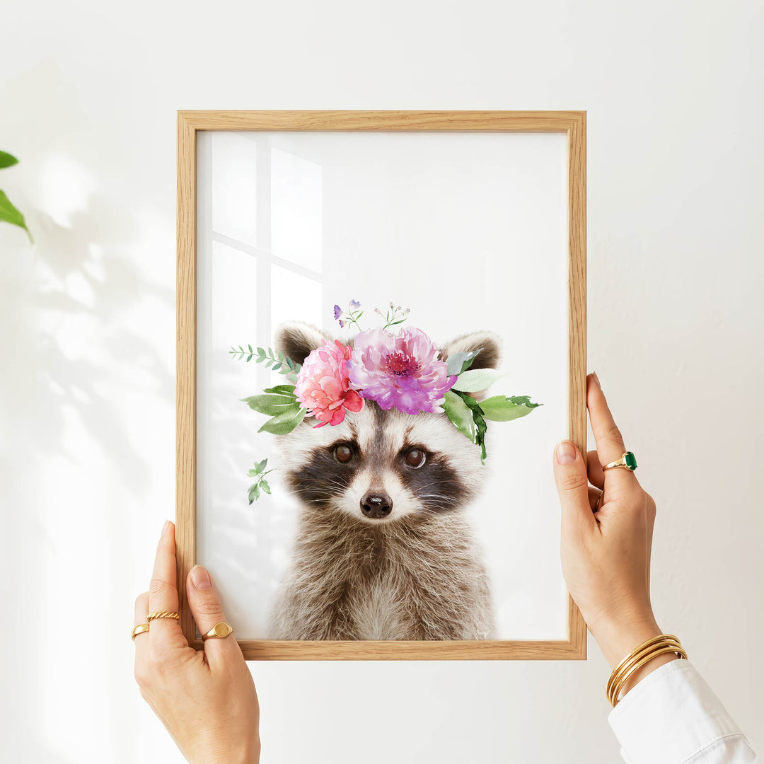 A person's hands are holding a wooden frame with a picture of a raccoon wearing a floral crown.