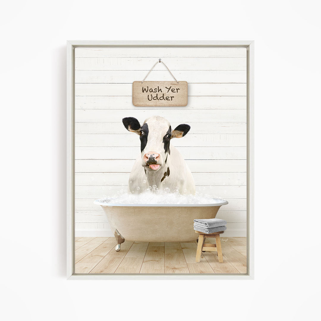 A black and white cow is sitting in a bathtub filled with water, with a sign above it that says "Wash Yer Udder".