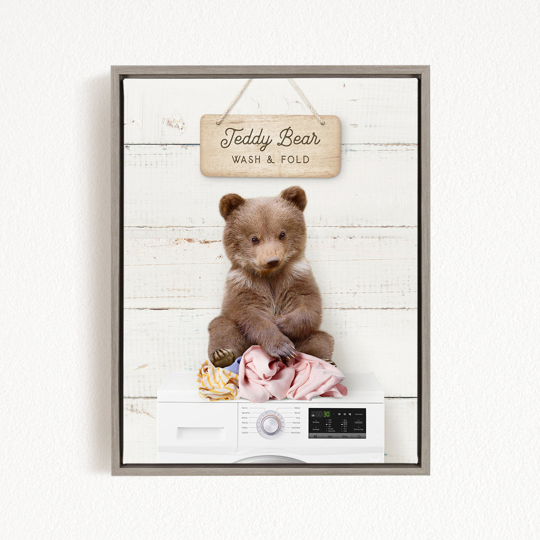 A framed image of a teddy bear sitting on a pile of laundry, with a sign above that says "Teddy Bear Wash & Fold".