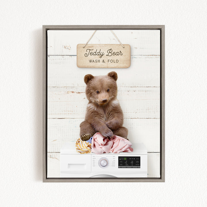 A framed image of a teddy bear sitting on a pile of laundry, with a sign above that says "Teddy Bear Wash & Fold".