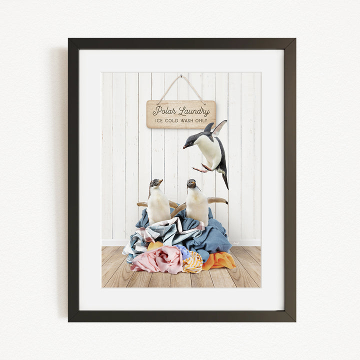 A framed image depicting two penguins sitting on a pile of clothes, with a sign that reads "Polar Laundry" above them.