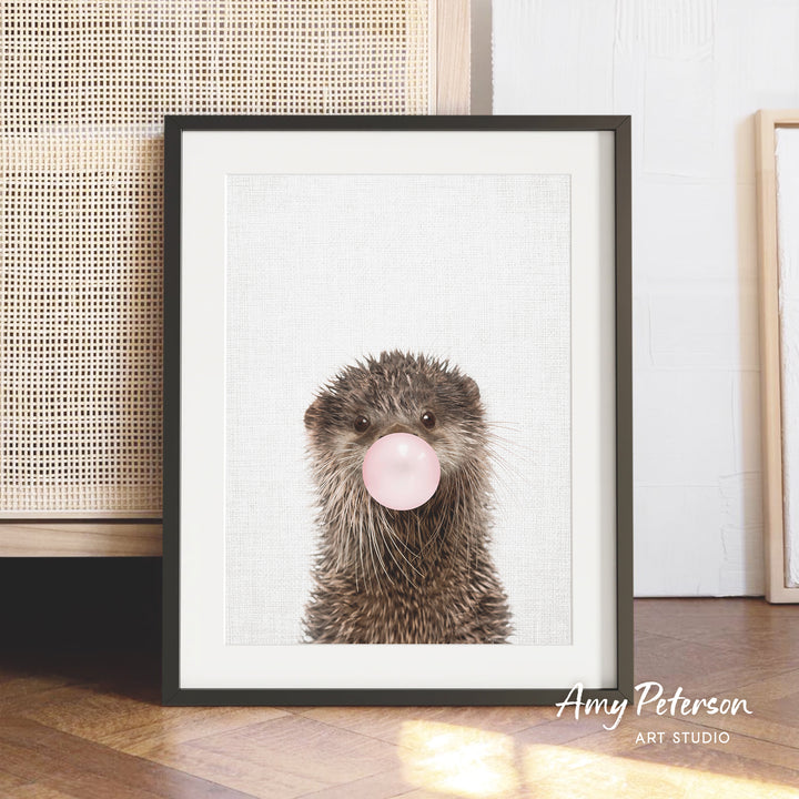 A framed image of an otter blowing a bubble with a pink bubble gum bubble.