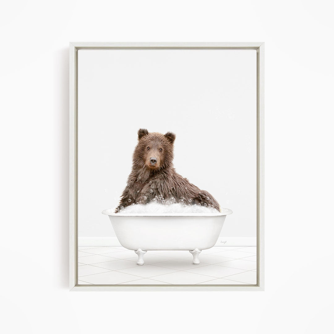 A brown bear sitting in a white bathtub filled with bubbles.