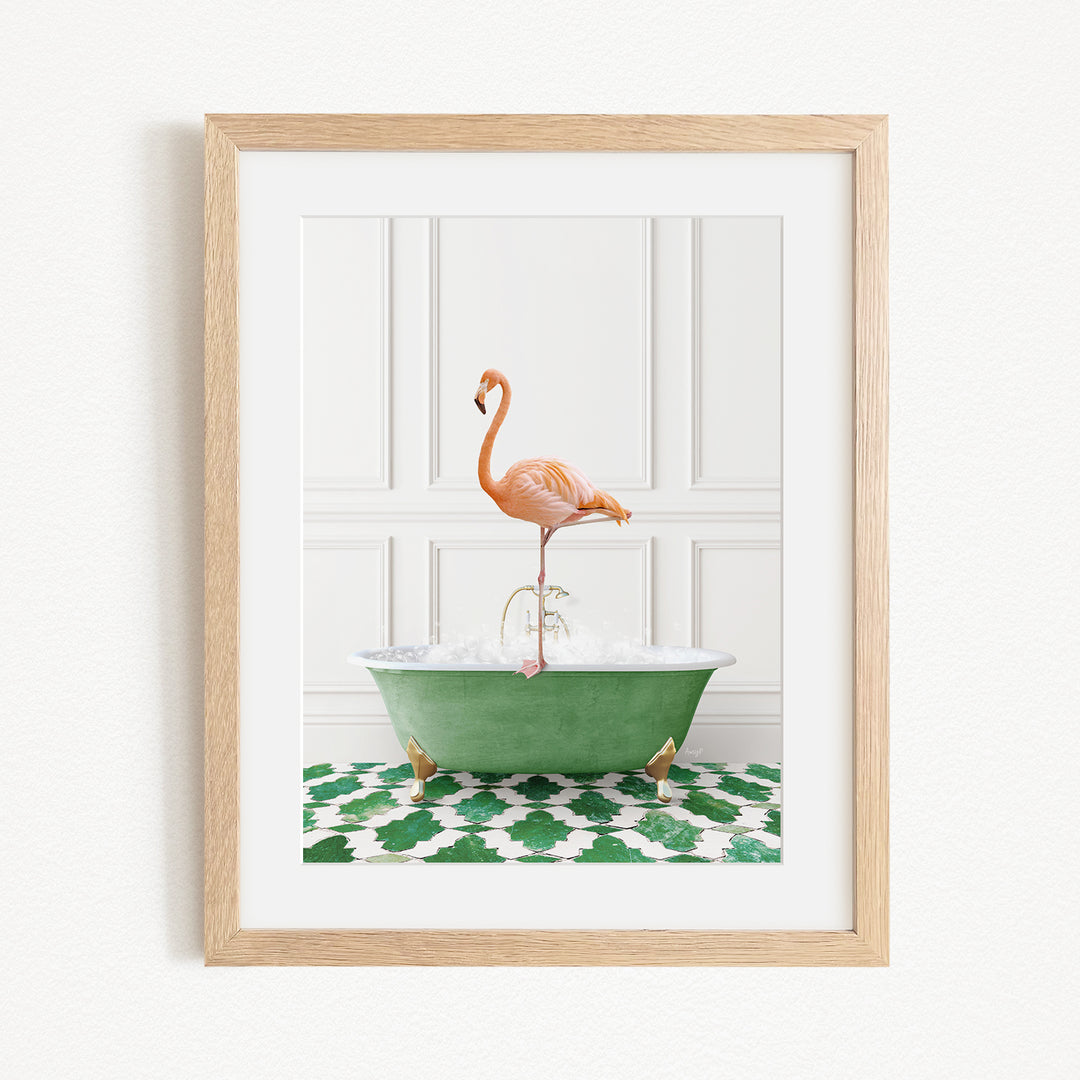 A framed image depicting a pink flamingo standing on a green bathtub filled with water, set against a white wall with a green and white patterned rug.