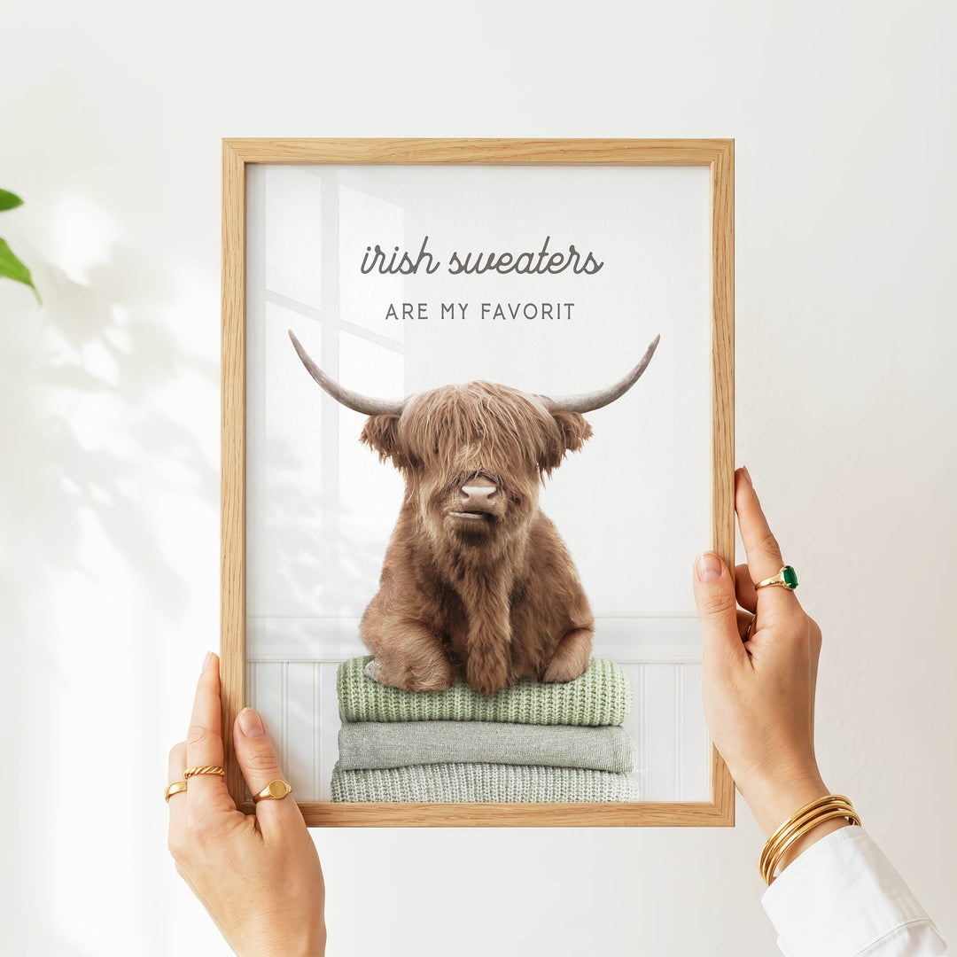 A person's hands are holding a framed picture of a brown cow with horns, which is sitting on a stack of green towels.