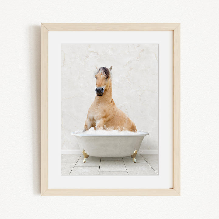 A light brown horse is sitting in a white bathtub filled with bubbles, looking directly at the camera.