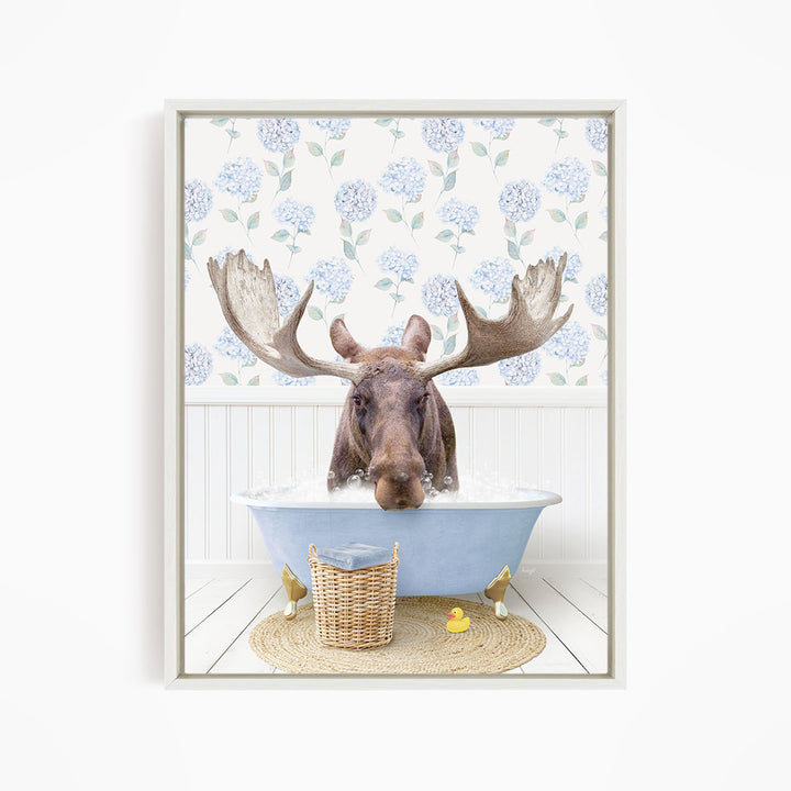 A moose with large antlers is sitting in a blue bathtub filled with water, surrounded by a wicker basket and yellow rubber ducks.