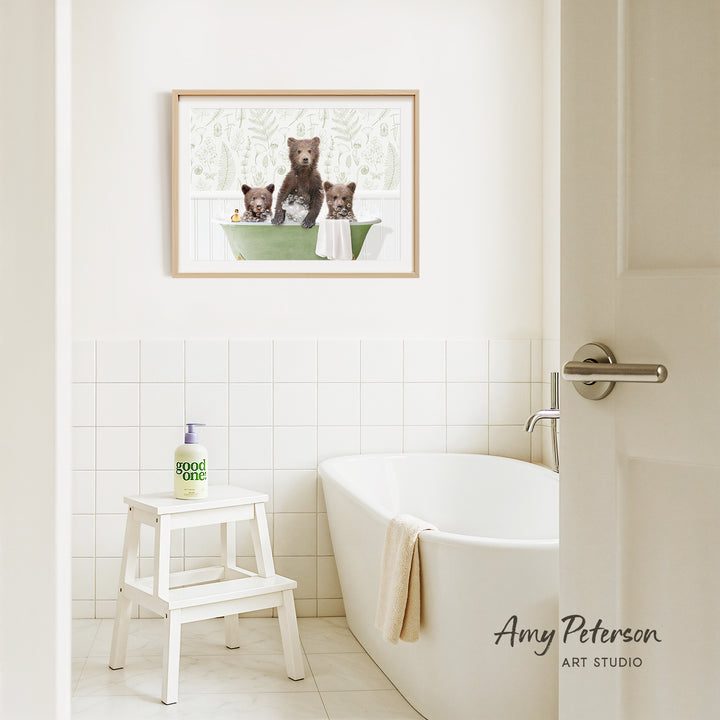 A framed image of three bears sitting in a bathtub is hanging on a white tiled wall above a white bathtub in a bathroom.