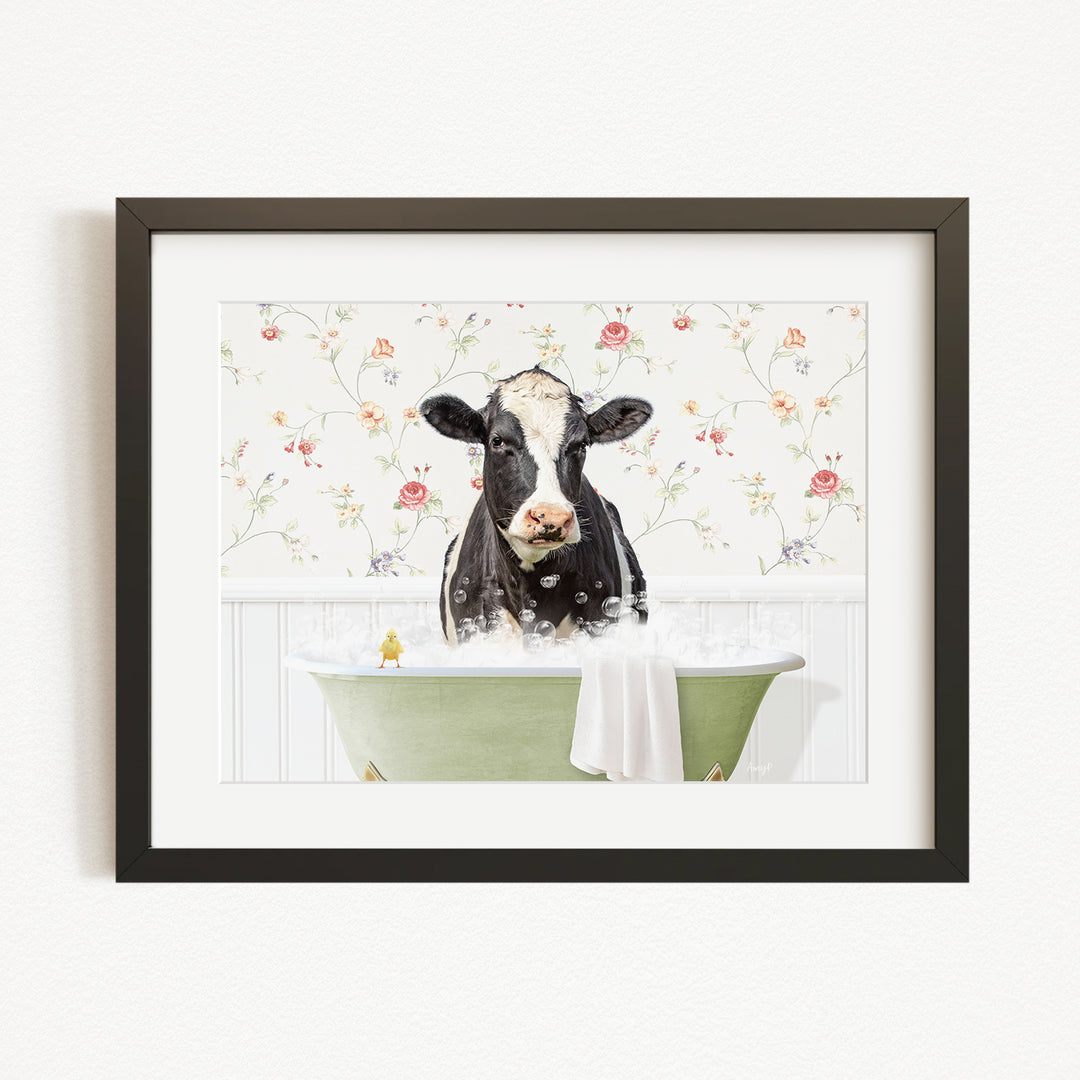 A black and white cow is sitting in a green bathtub filled with bubbles, surrounded by a floral patterned wall.