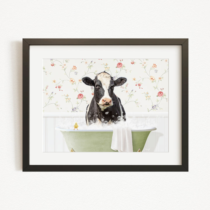 A black and white cow is sitting in a green bathtub filled with bubbles, surrounded by a floral patterned wall.