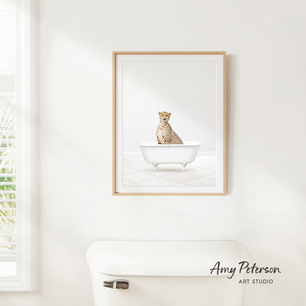 A cheetah sitting in a white bathtub, as depicted in a framed artwork hanging on a white wall.