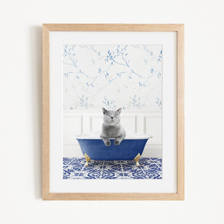 A gray cat sitting in a blue bathtub, with a blue and white patterned tile floor and a floral wallpaper in the background.